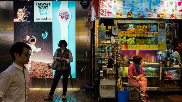 Жена използва мобилния си телефон пред реклама на Swatch в Хонконг, Китай; Photographer: Billy H.C. Kwok/Bloomberg
