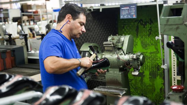 Служител в цех използва чук, за да прикрепи подметката на дамска обувка Снимка: Paulo Duarte/Bloomberg